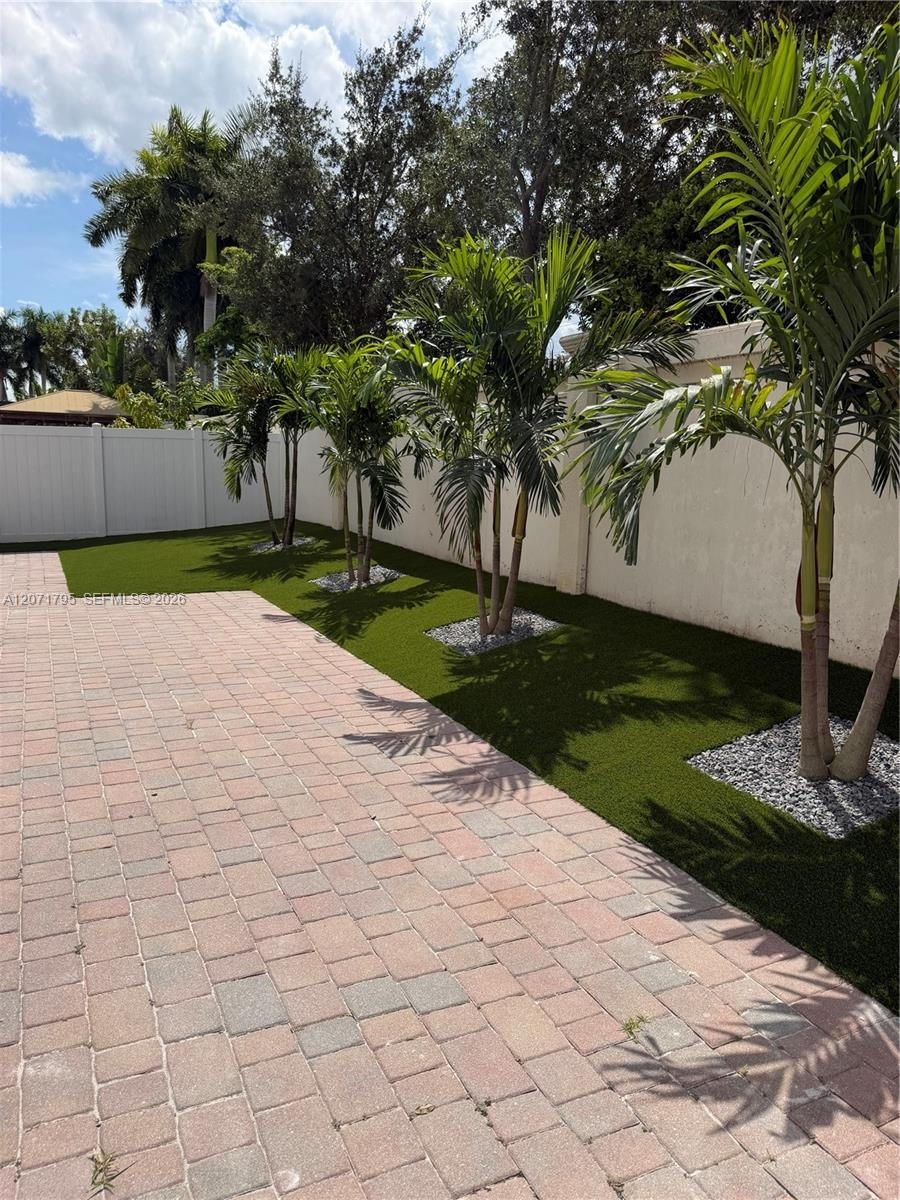 Outdoor patio featuring concrete pavers, synthetic turf, mature palm trees, decorative stone mulch, and a privacy wall
