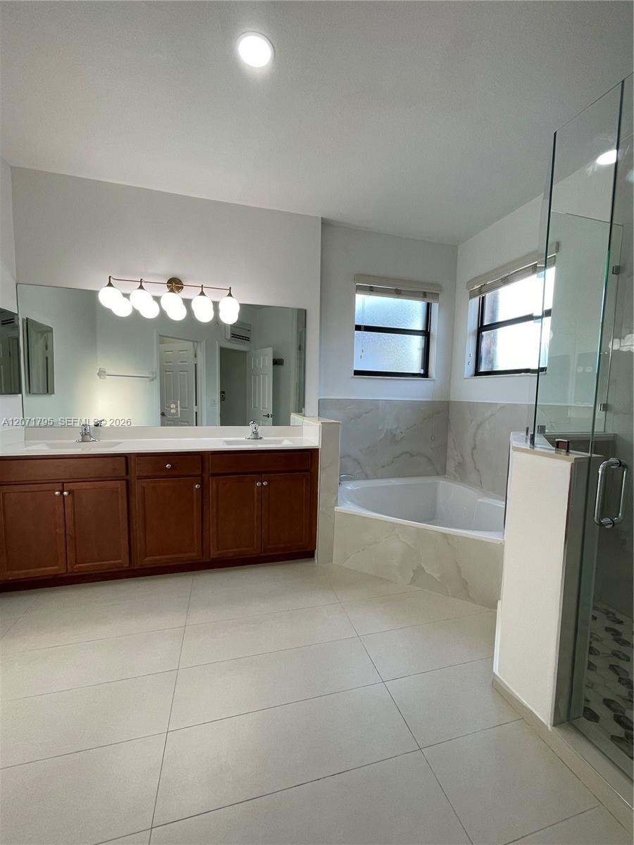 Bathroom featuring a double-sink vanity with wood cabinetry, a large wall-mounted mirror, a separate glass-enclosed shower, and a built-in soaking tub