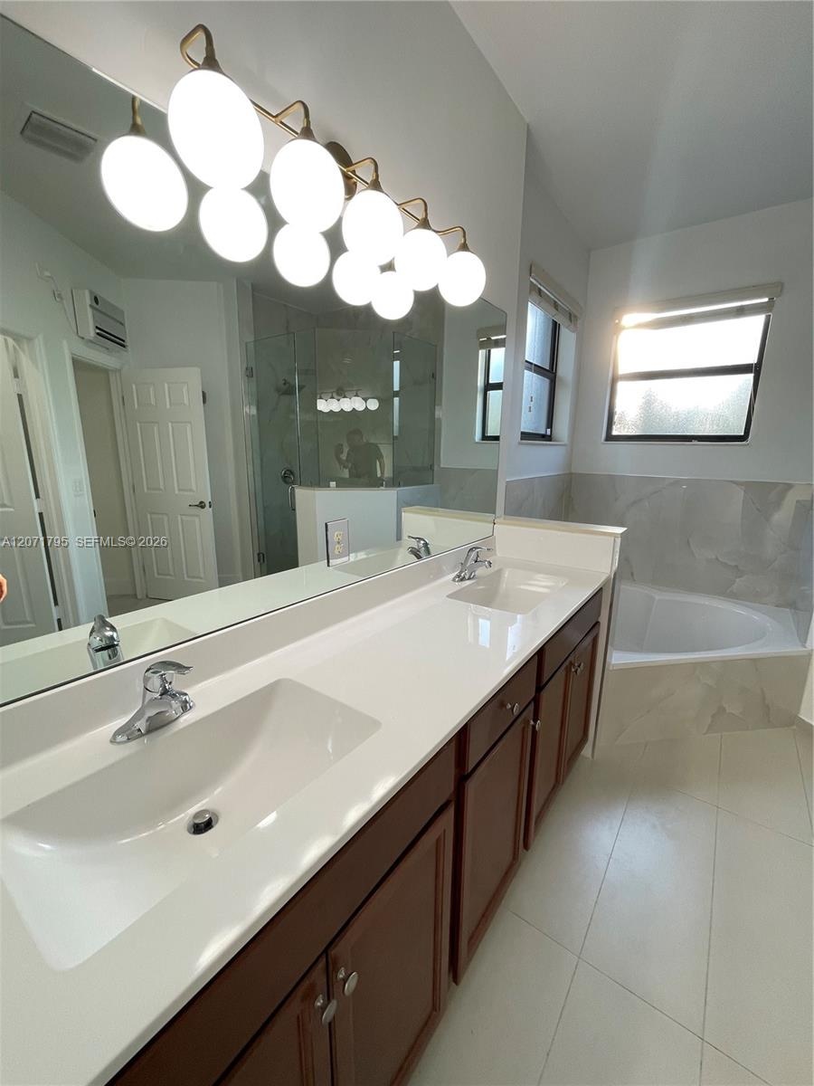 Dual-sink vanity with a solid-surface countertop, dark wood-finish cabinetry, large wall-mounted mirror, multi-globe light fixture, and corner soaking
