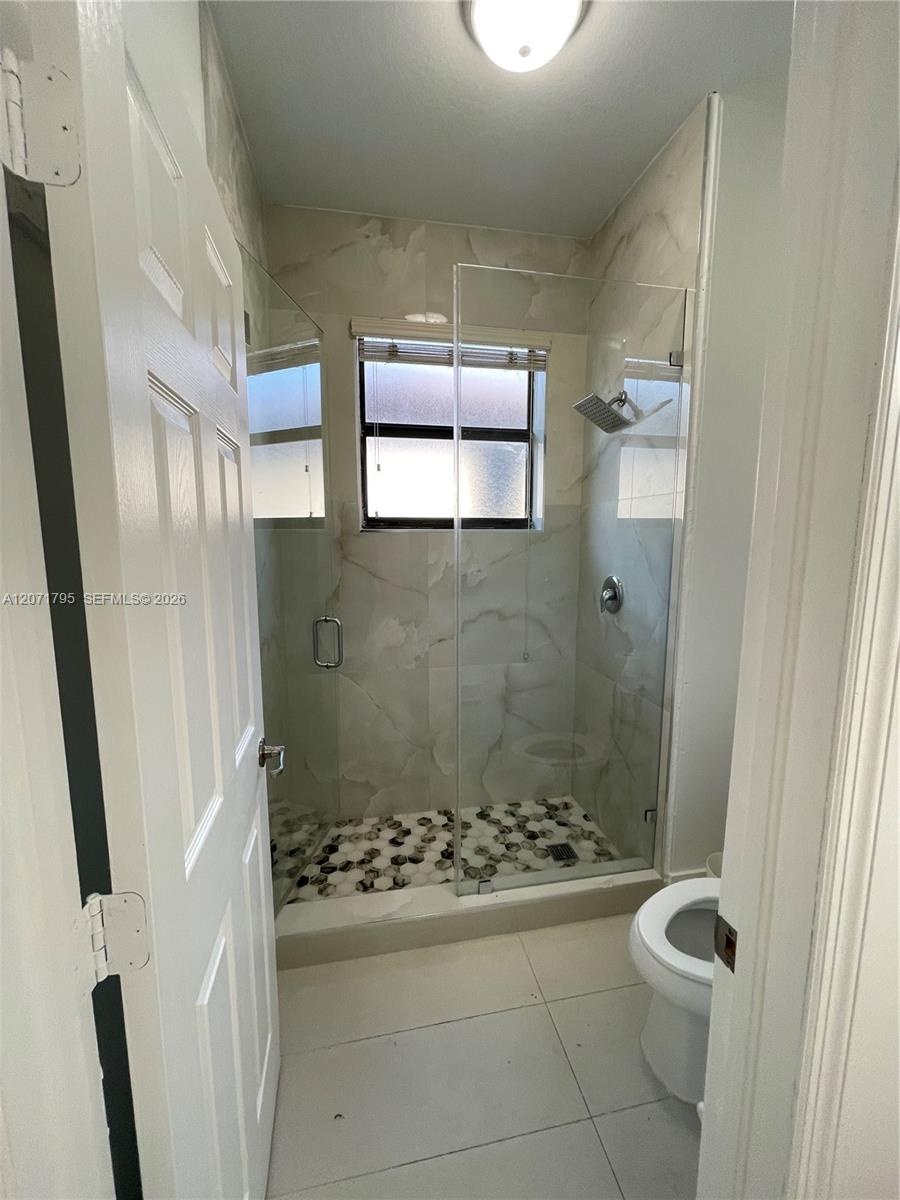 Walk-in shower featuring floor-to-ceiling tile, a frameless glass enclosure, pebble-stone shower floor, and a wall-mounted shower head, complemented b