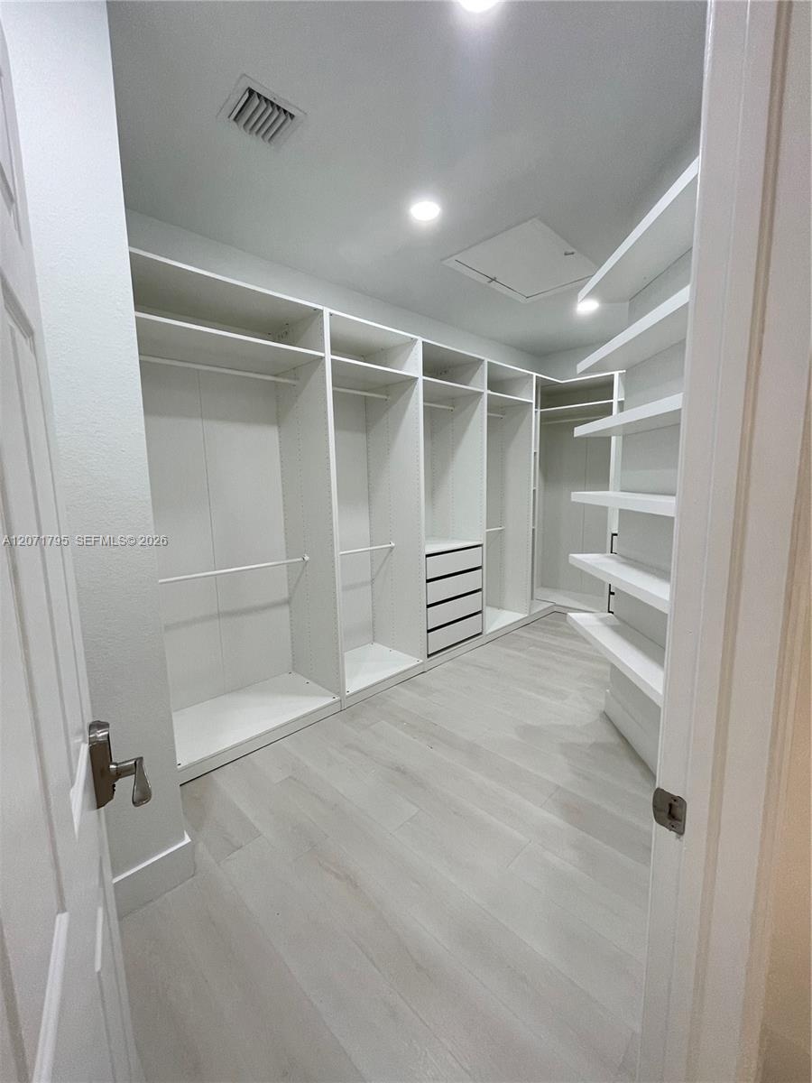 Walk-in closet featuring floor-to-ceiling white custom built-in cabinetry, integrated drawer storage, open shelving, and wood-finish flooring