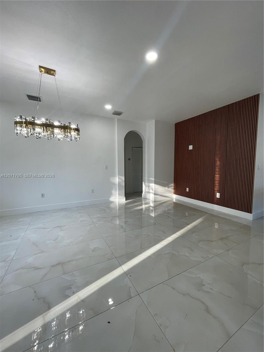 Large-format polished tile flooring, vertical wood-slat accent wall, recessed lighting, crystal-style chandelier, and arched doorway