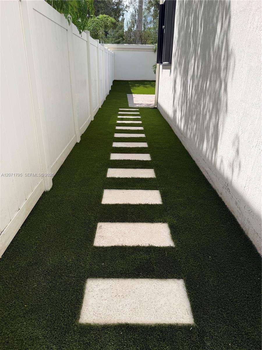 Side yard featuring synthetic turf, concrete paver stones, and white vinyl privacy fencing