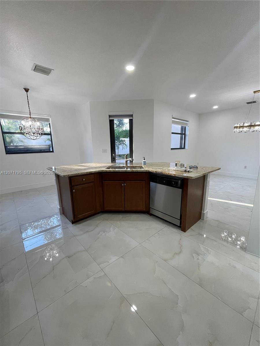Kitchen island featuring wood cabinetry, stone-finish countertops, stainless steel undermount sink, and integrated stainless steel dishwasher, complem