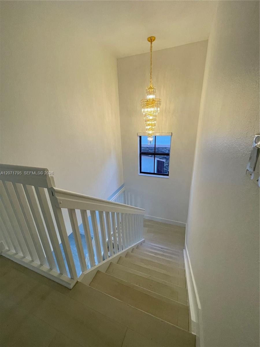 Staircase featuring wood-finish treads, a white wooden balustrade, and a multi-tiered crystal chandelier pendant fixture