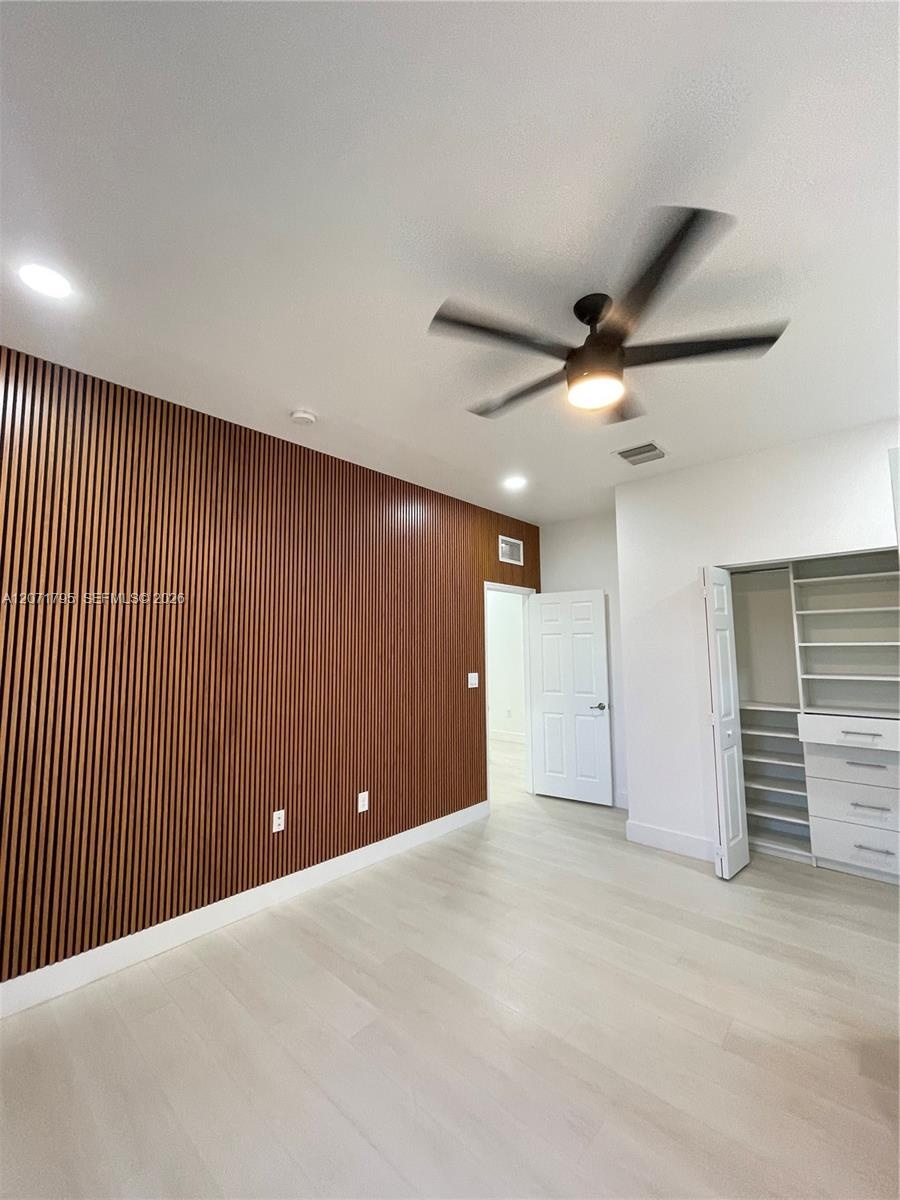 Interior space featuring a slatted wood-finish accent wall, light-toned wood-finish flooring, recessed lighting, and a modern ceiling fan with an inte