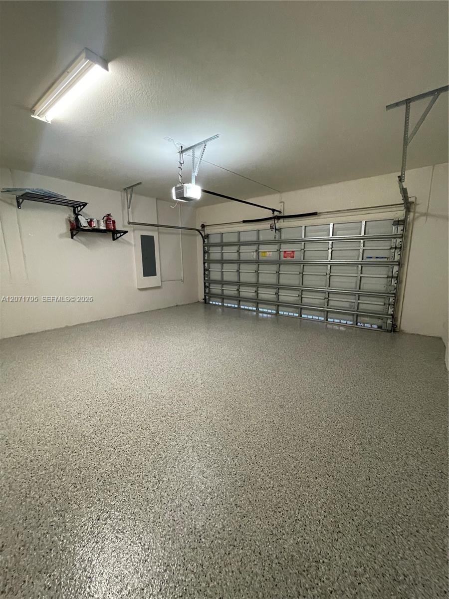 Garage space featuring an epoxy-coated floor finish, motorized overhead door, wall-mounted storage shelving, and fluorescent overhead lighting