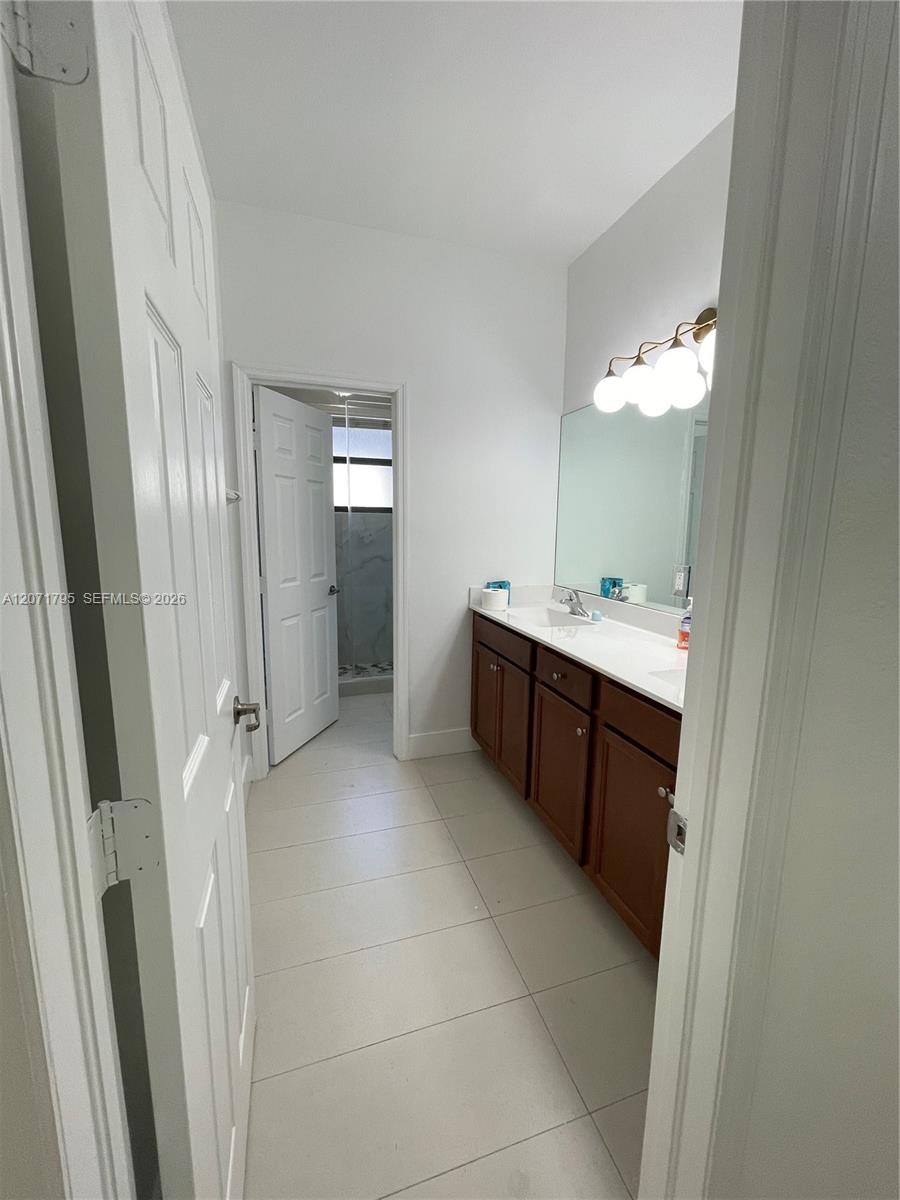 Bathroom featuring a dual-sink vanity with wood-finish cabinetry, solid surface countertop, large wall-mounted mirror, and multi-globe vanity lighting
