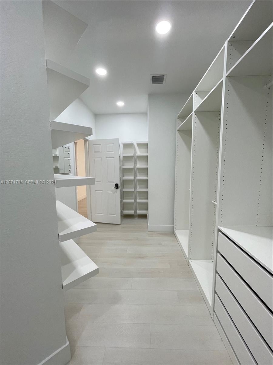 Walk-in storage area featuring custom white built-in shelving, integrated dresser drawers, recessed lighting, and wood-finish flooring