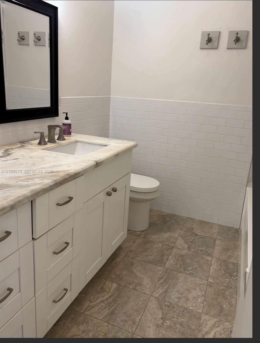 White vanity with a stone countertop, under-mount sink, subway tile wainscoting, and large-format tile flooring