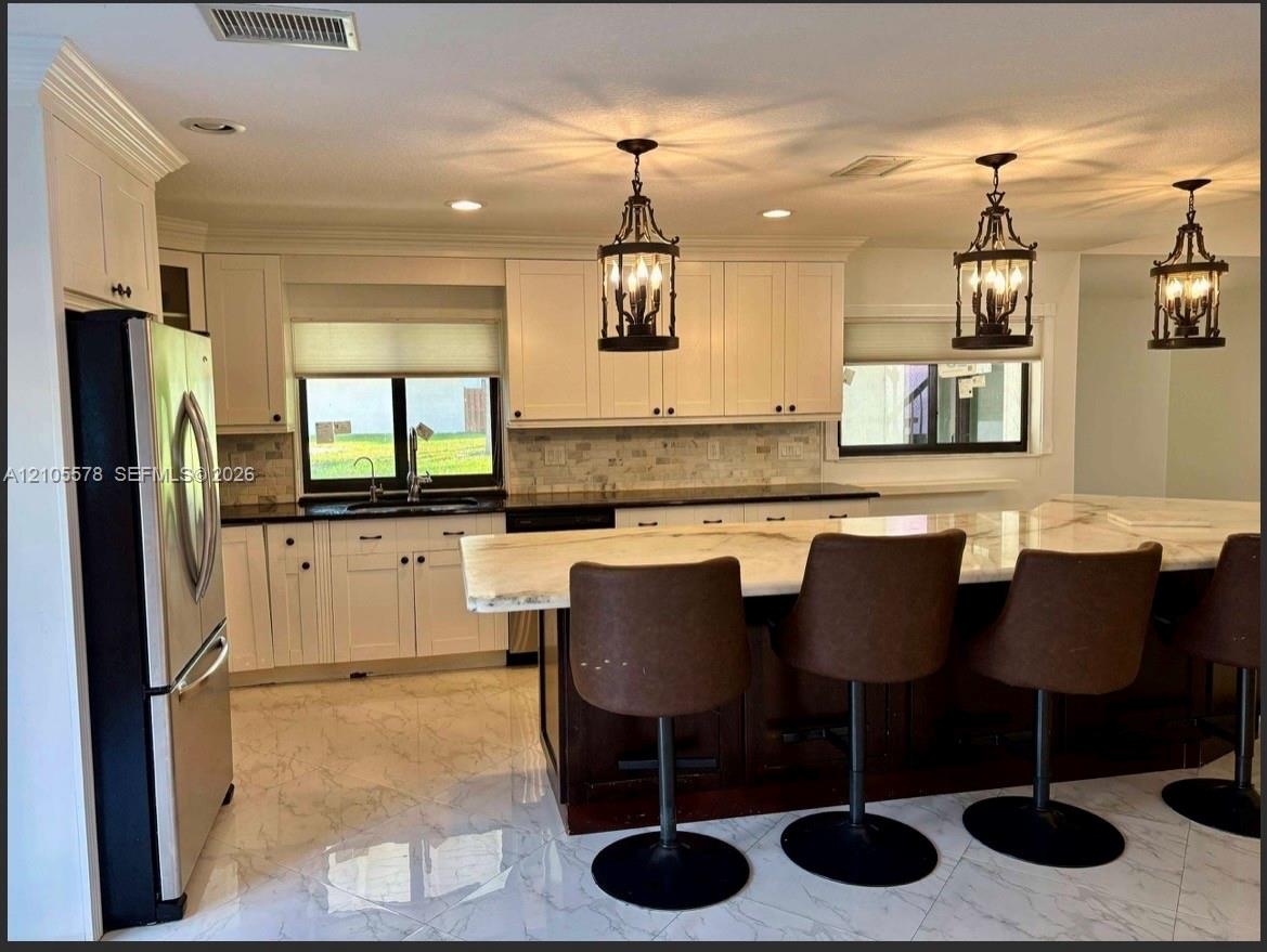 Kitchen featuring white shaker cabinetry, stone-topped central island with seating, stone backsplash, stainless steel appliances, and polished tile fl
