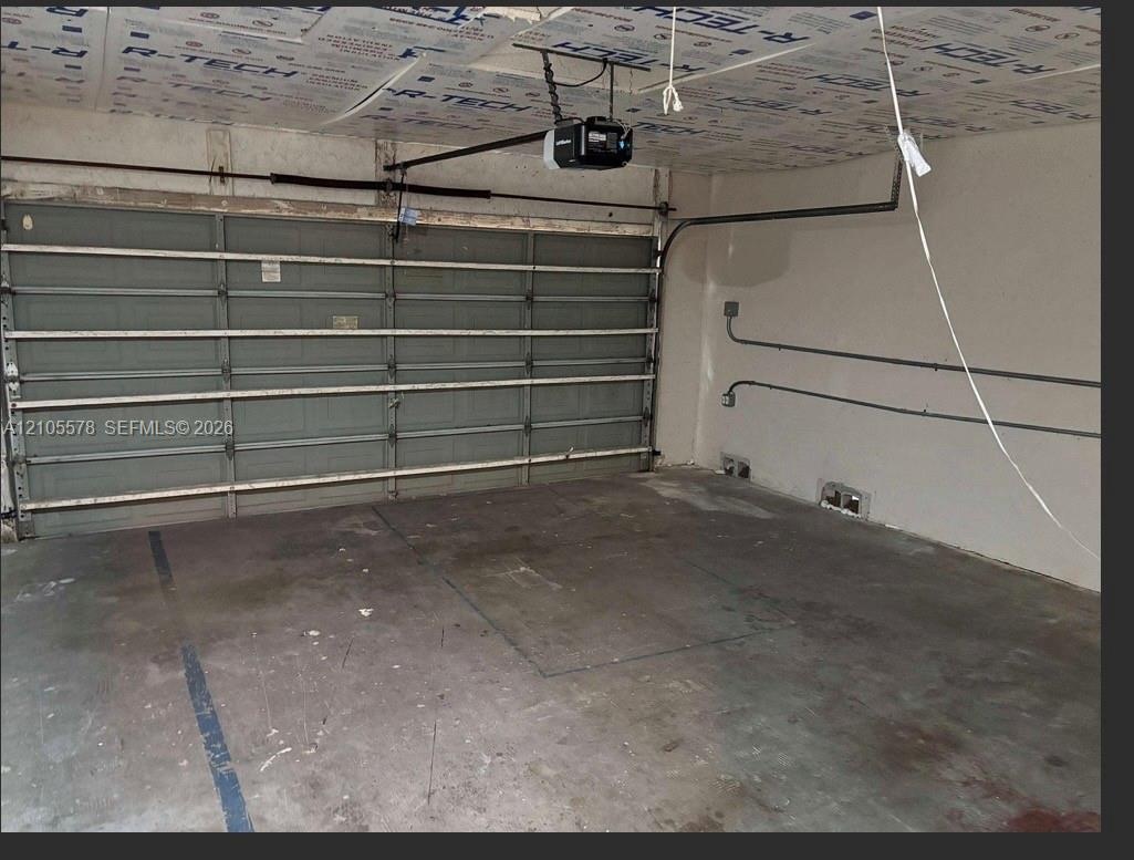 Multi-car garage featuring a sectional overhead door, automated door opener, and exposed interior wall conduit