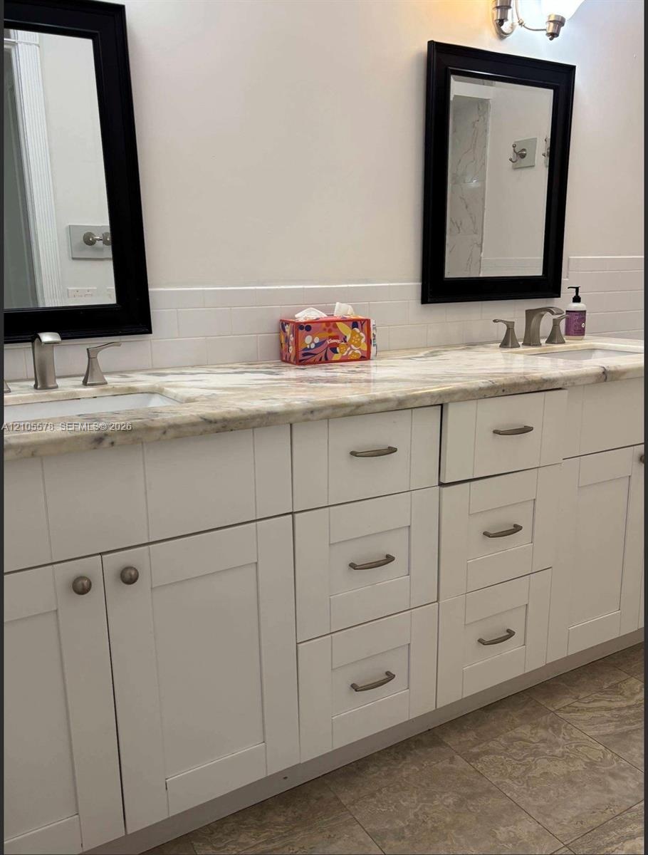Dual-vanity bathroom featuring a light-toned stone countertop, white shaker-style cabinetry, undermount sinks, and dual black-framed wall mirrors