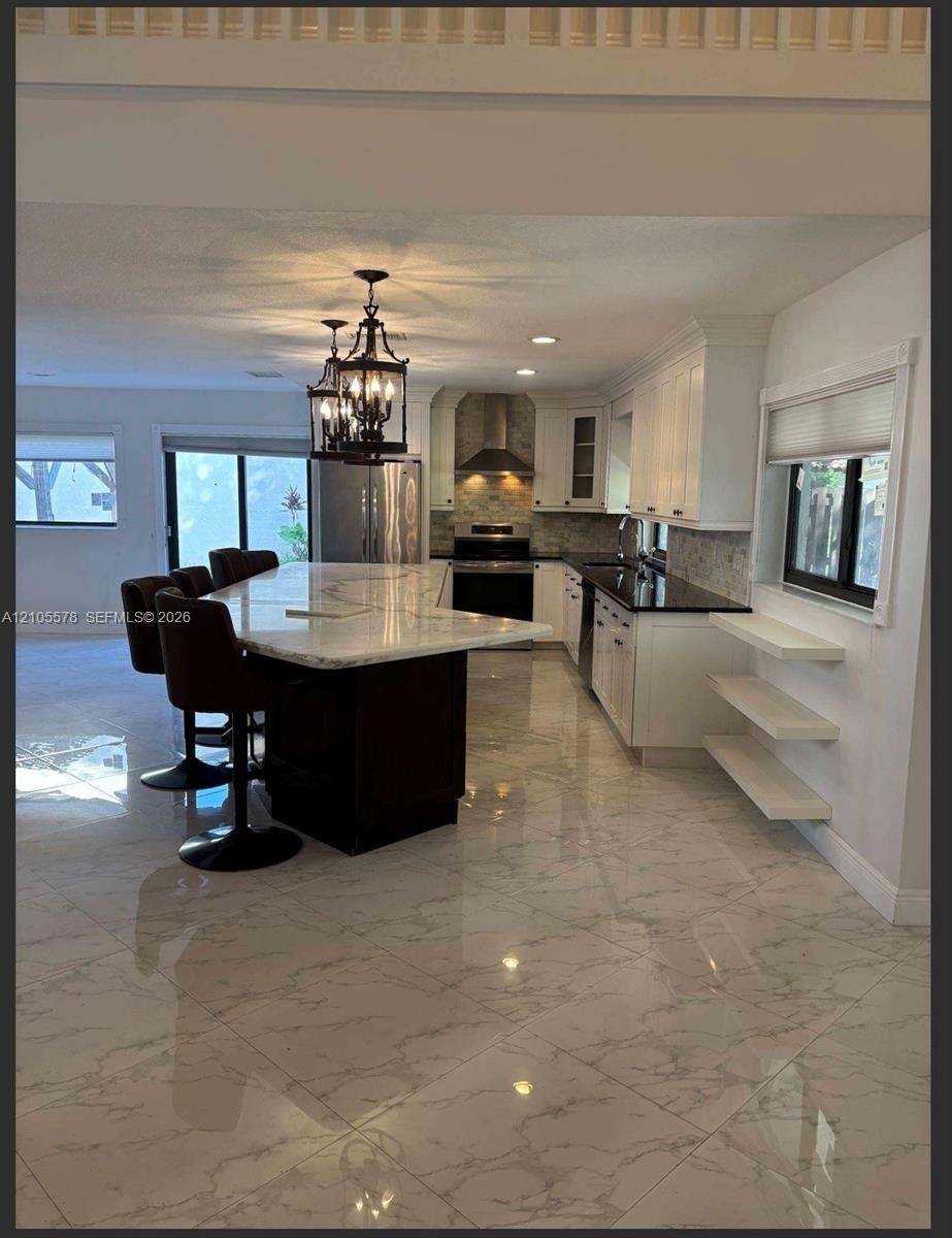 Kitchen featuring a large central island with light-toned stone-finish countertop, white cabinetry, dark stone-finish perimeter counters, polished til