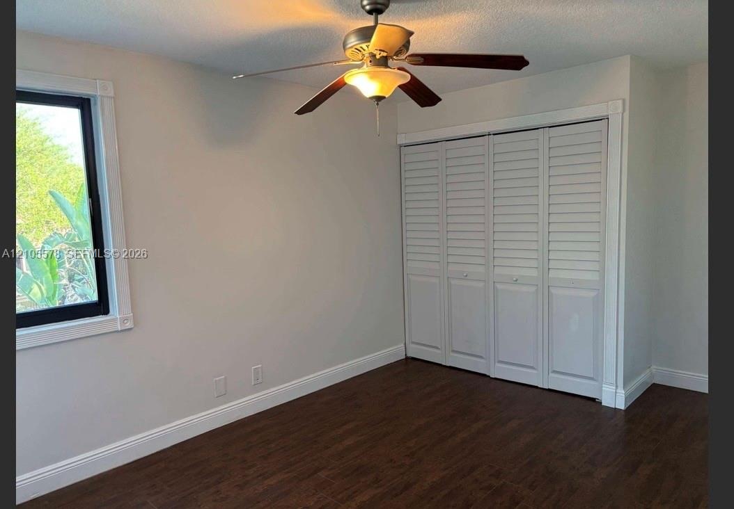 Interior room featuring wood-finish flooring, a multi-pane window with white trim, a ceiling fan with integrated lighting, and a bi-fold louvered clos