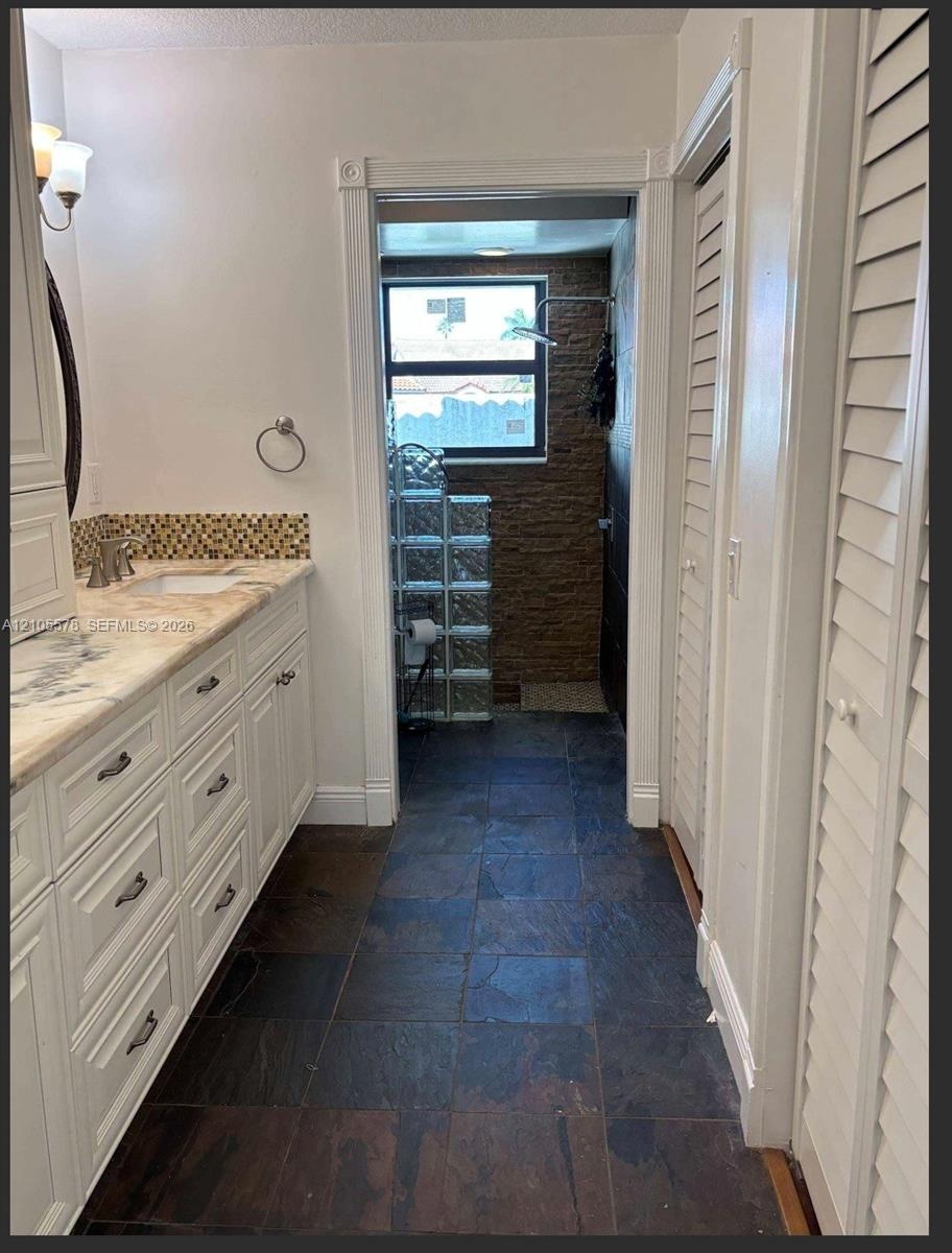 Bathroom featuring a white cabinetry vanity, stone-patterned countertop with a mosaic tile backsplash, slate-finish floor tile, and a textured stone w