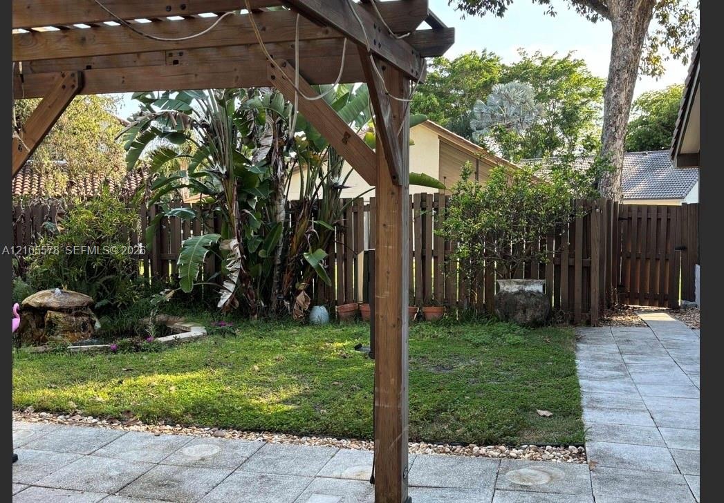 Backyard featuring a wooden pergola, stone-tile patio, wood privacy fencing, a stone water feature, and mature tropical landscaping