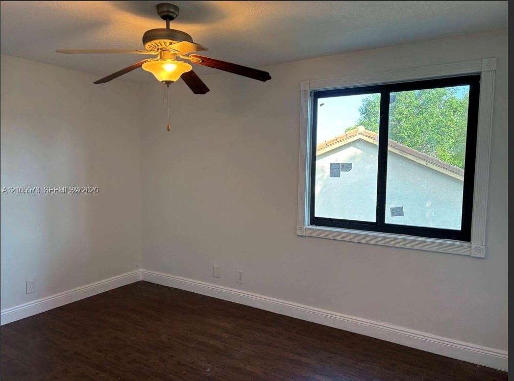 Room featuring dark wood-finish flooring, a ceiling fan with integrated lighting, and a window framed by white molding
