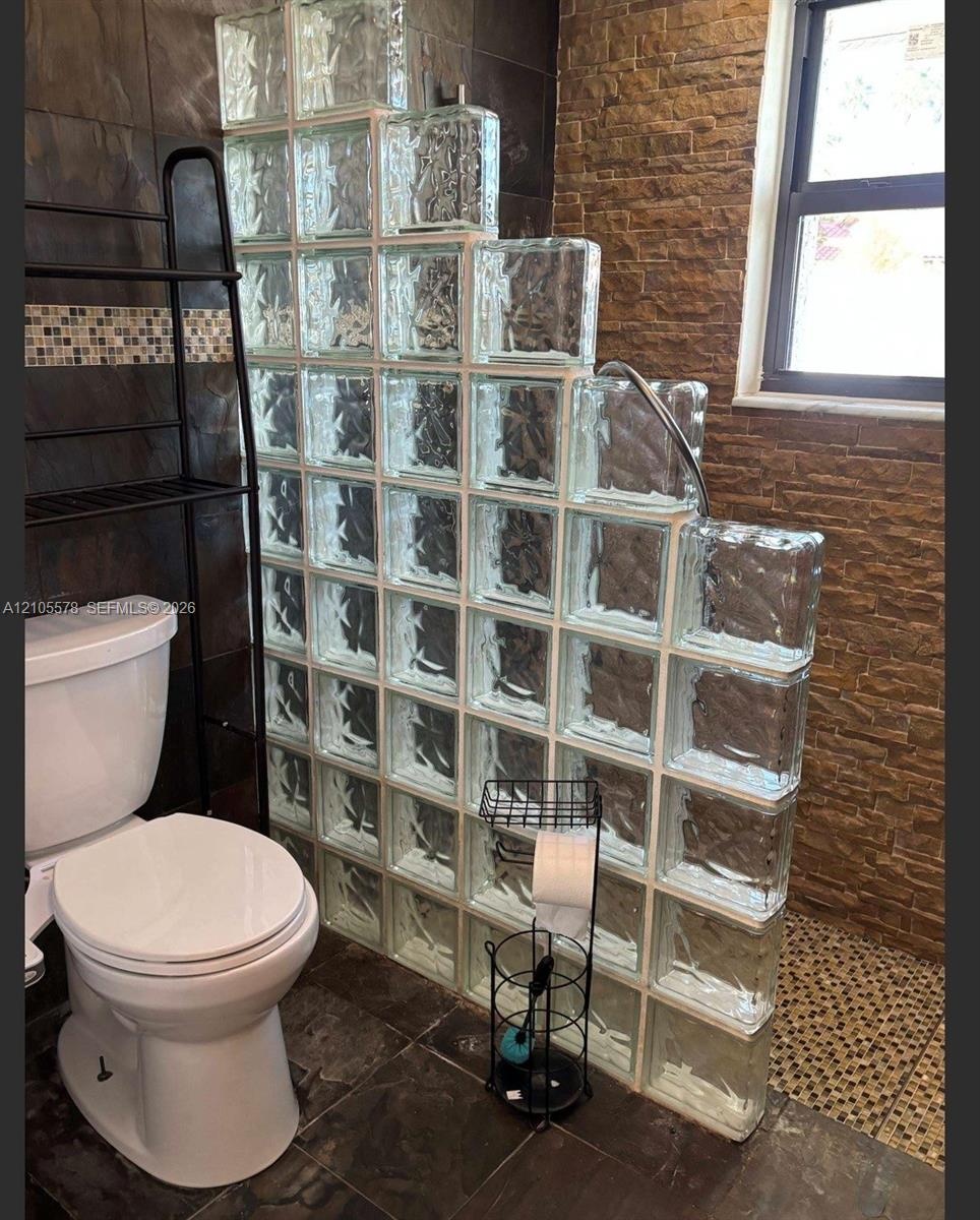 Glass block privacy partition, textured stone-finish wall, dark oversized tile flooring, and a single-hung window