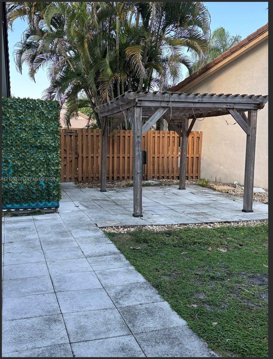Rear exterior space featuring a wooden pergola, concrete paver patio, tall wooden privacy fencing, and established palm trees