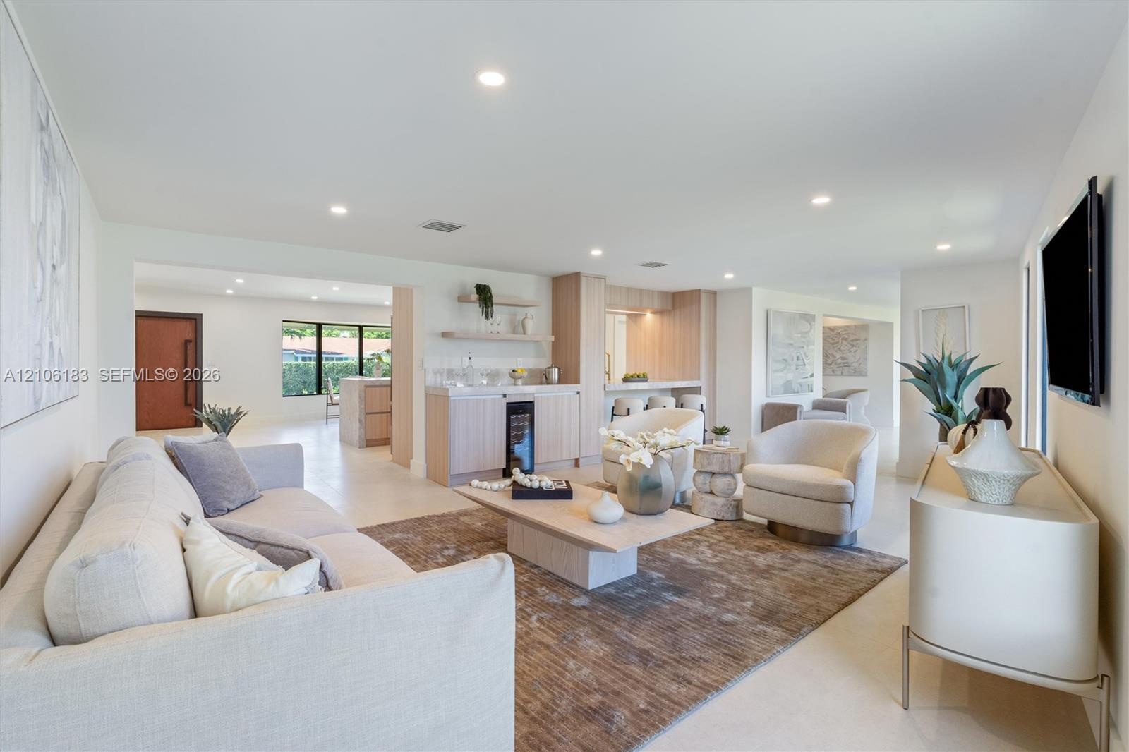 Open-concept interior featuring light-toned neutral flooring, recessed lighting, and a built-in wet bar with a glass-front beverage refrigerator and o