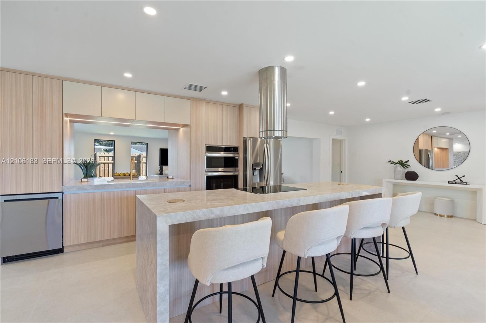 Contemporary kitchen featuring a large waterfall-edge island with light stone countertops, stainless steel appliances including a built-in double oven