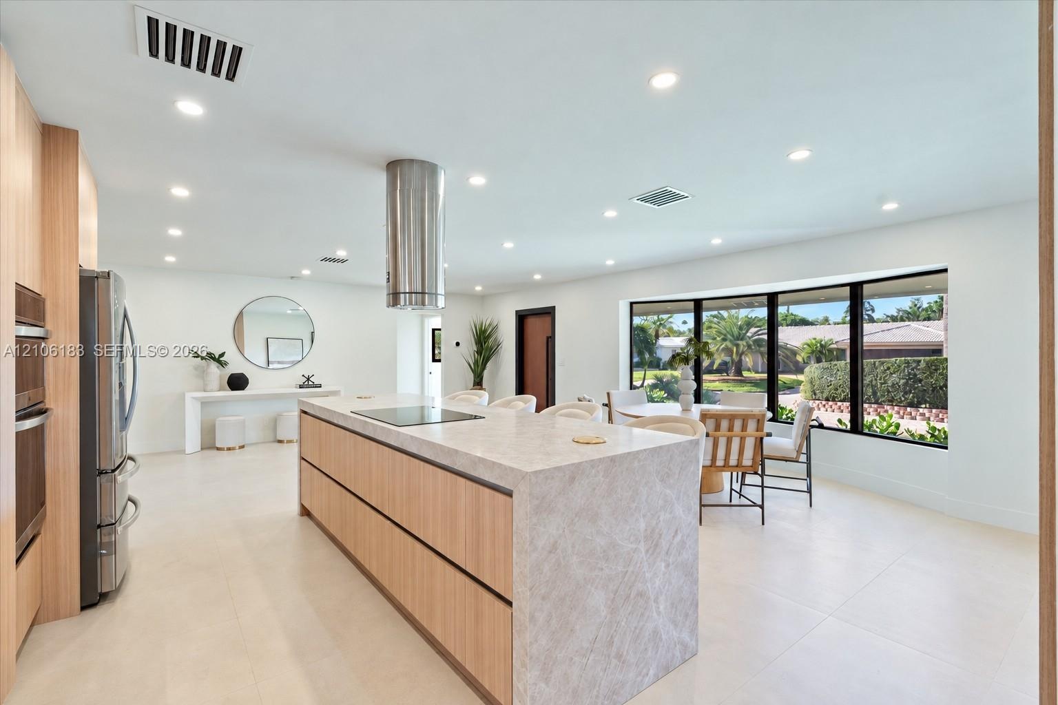 Kitchen featuring a central island with a waterfall-edge stone countertop, cylindrical stainless steel range hood, built-in wall oven, flat-panel cabi