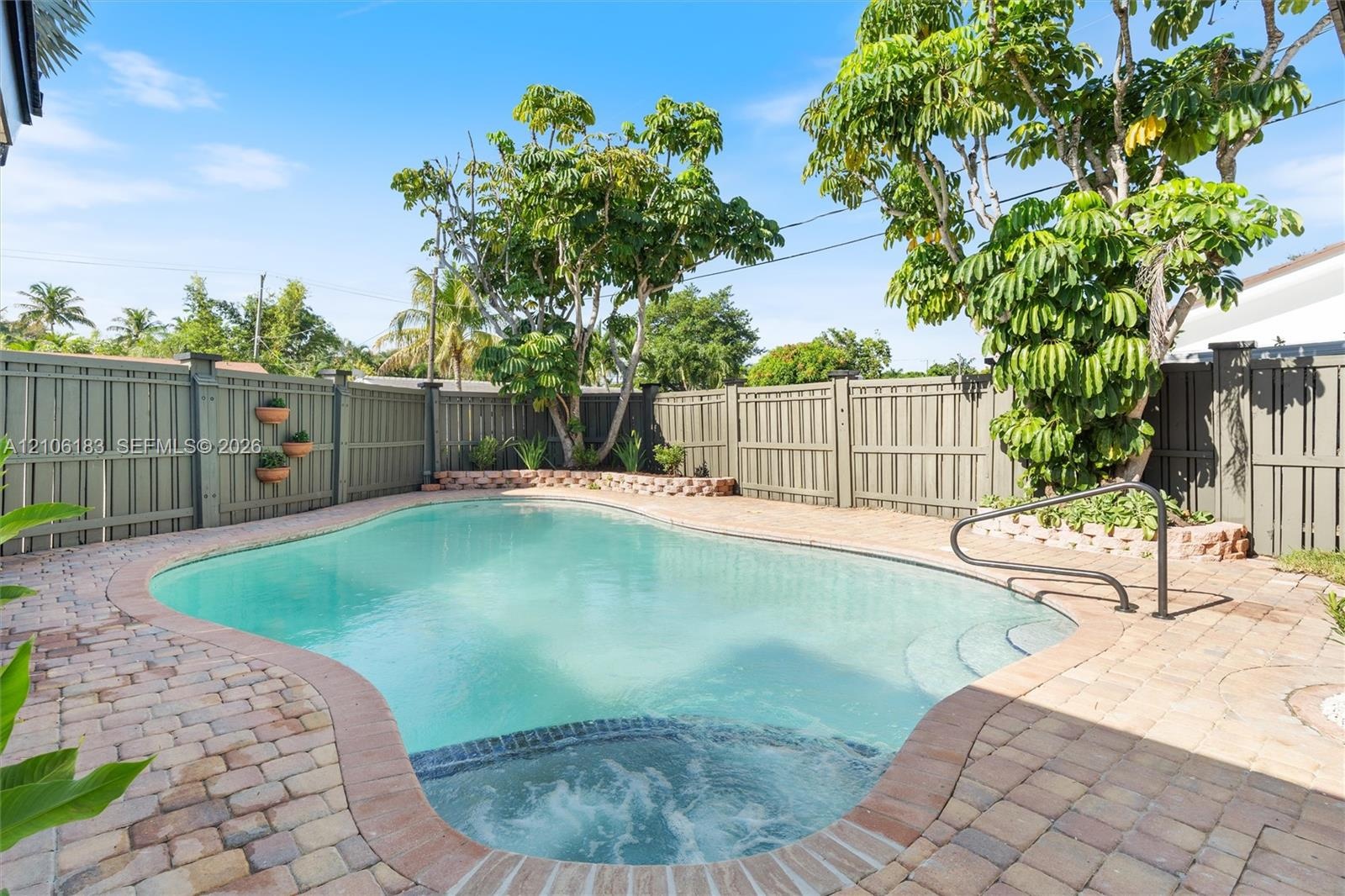 In-ground pool with integrated spa, bordered by paver decking and enclosed by perimeter fencing with mature landscaping
