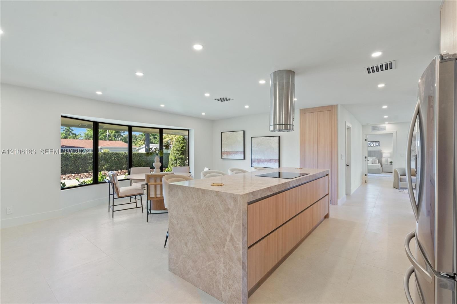 Kitchen featuring a waterfall-edge center island, stone countertops, flat-panel light wood cabinetry, a cylindrical stainless steel range hood, and la