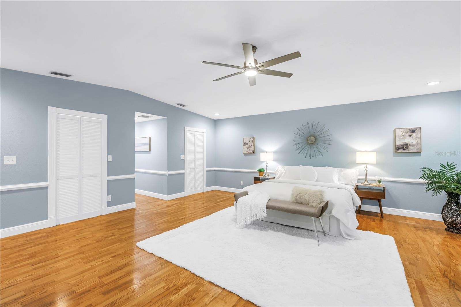 Exquisite primary bedroom suite featuring dual expansive walk-in closets, vaulted ceilings, a dedicated sitting area, hardwood flooring, and a private