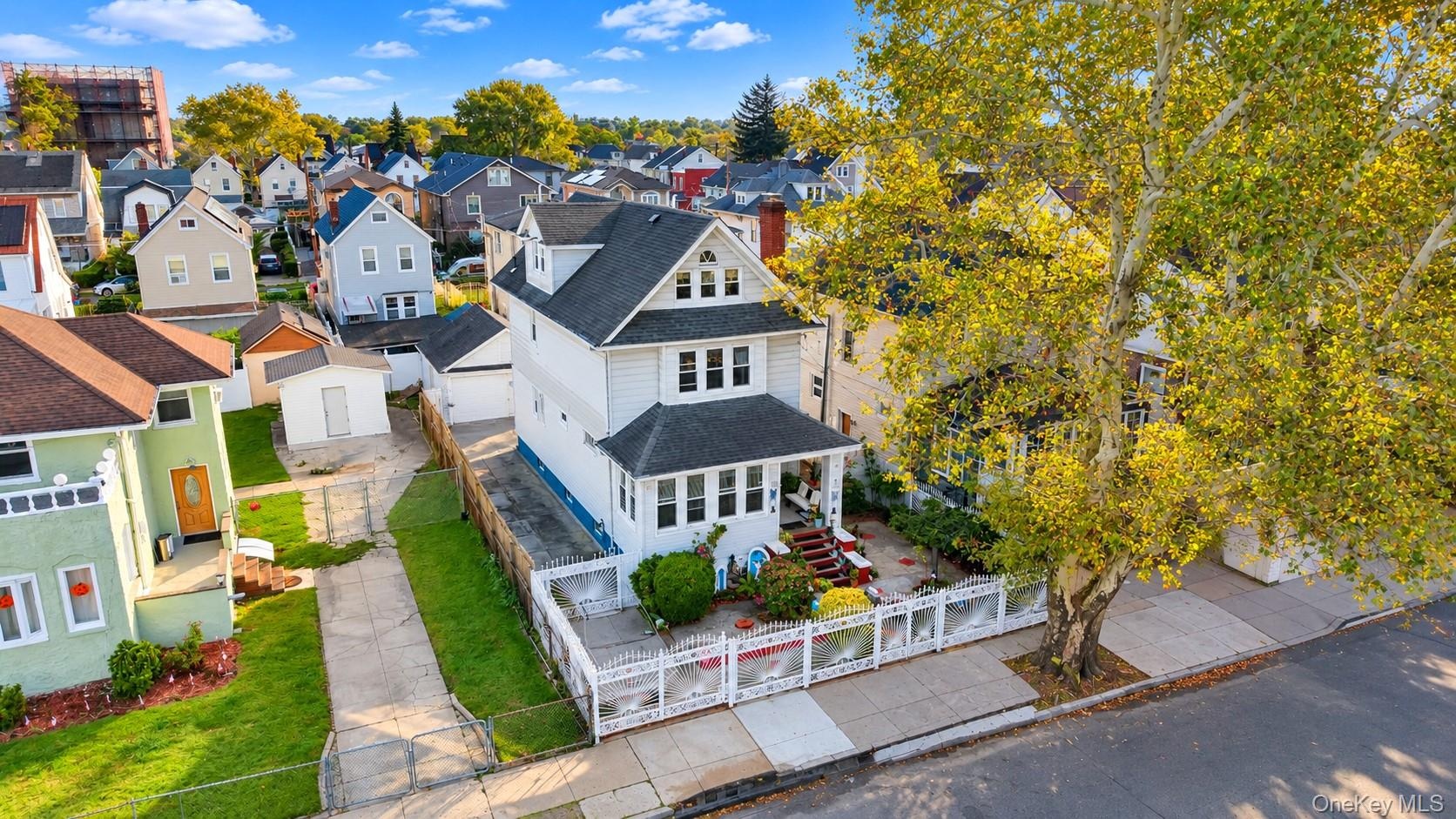 Three-story residence featuring a covered front porch, white siding, a paved driveway, and a fenced front yard with mature landscaping