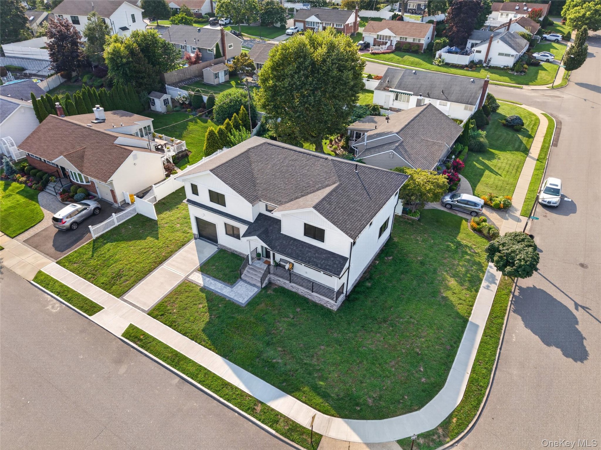 Corner lot property featuring two-tone exterior siding, stone veneer base, shingled roof, concrete driveway, and a paved walkway