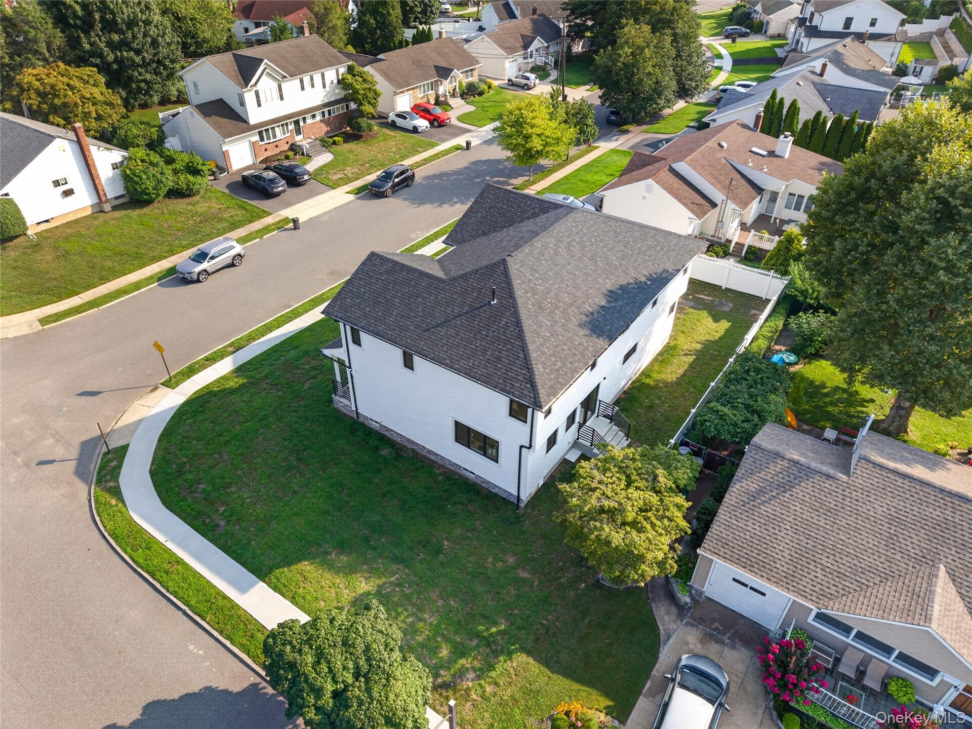 Corner lot featuring a multi-level structure with a gabled roof, white siding, and a fenced rear perimeter