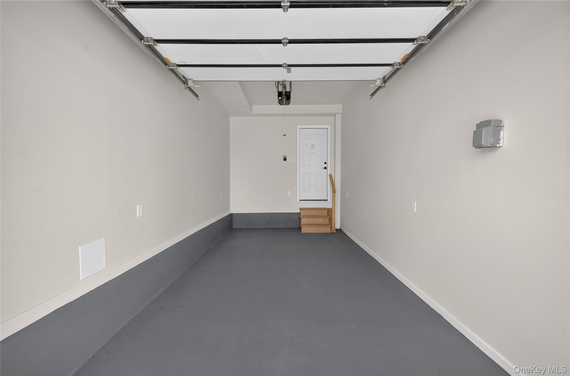 Finished garage featuring an epoxy-coated floor, overhead door mechanism, neutral wall paint, and an elevated entry door with interior steps