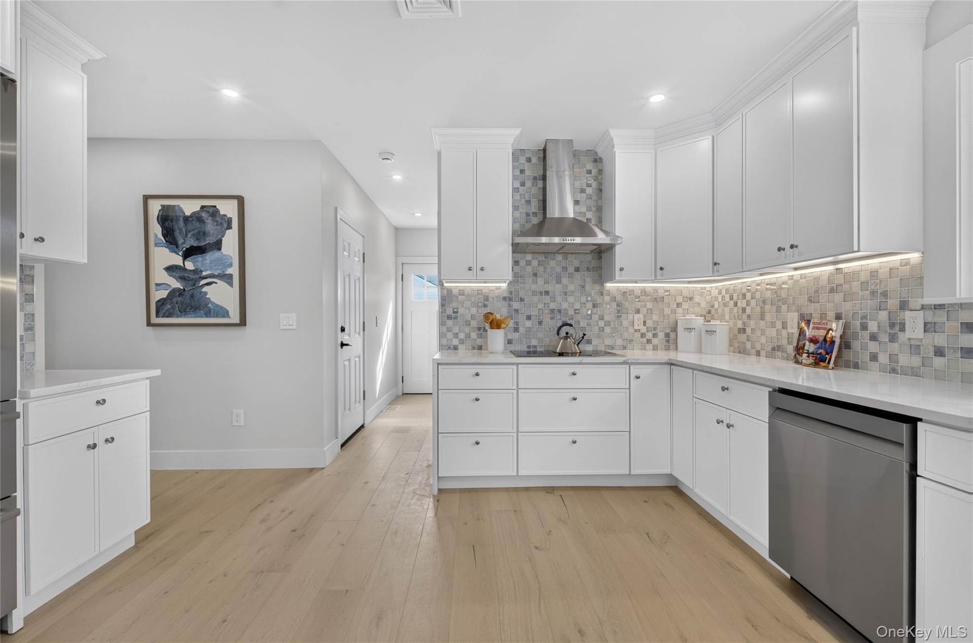 Kitchen featuring white shaker-style cabinetry, quartz countertops, a mosaic tile backsplash, stainless steel range hood, and wood-finish flooring