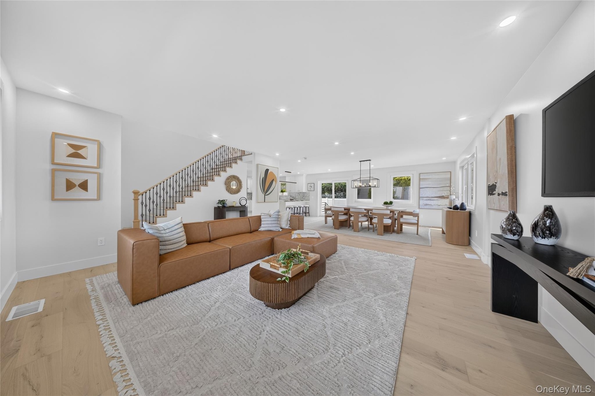 Open-concept living space featuring wood-finish flooring, recessed lighting, and a staircase with an iron-baluster railing