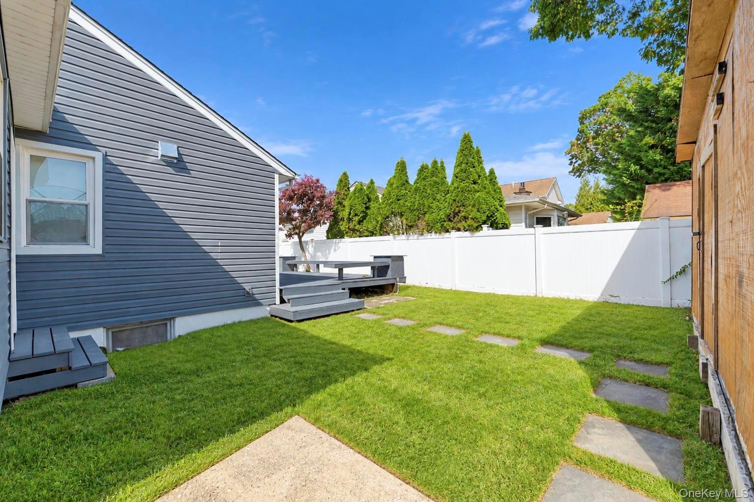 Backyard featuring horizontal siding, a multi-level deck, stone paver walkway, and full-height vinyl fencing