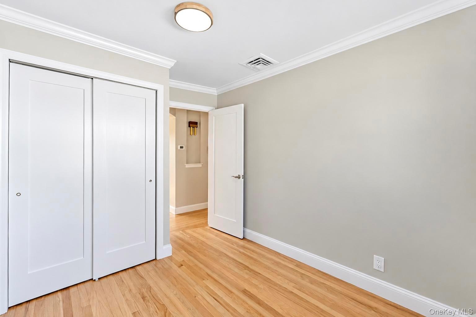 Room featuring wood-finish flooring, white panel doors, dual sliding closet doors, and crown molding