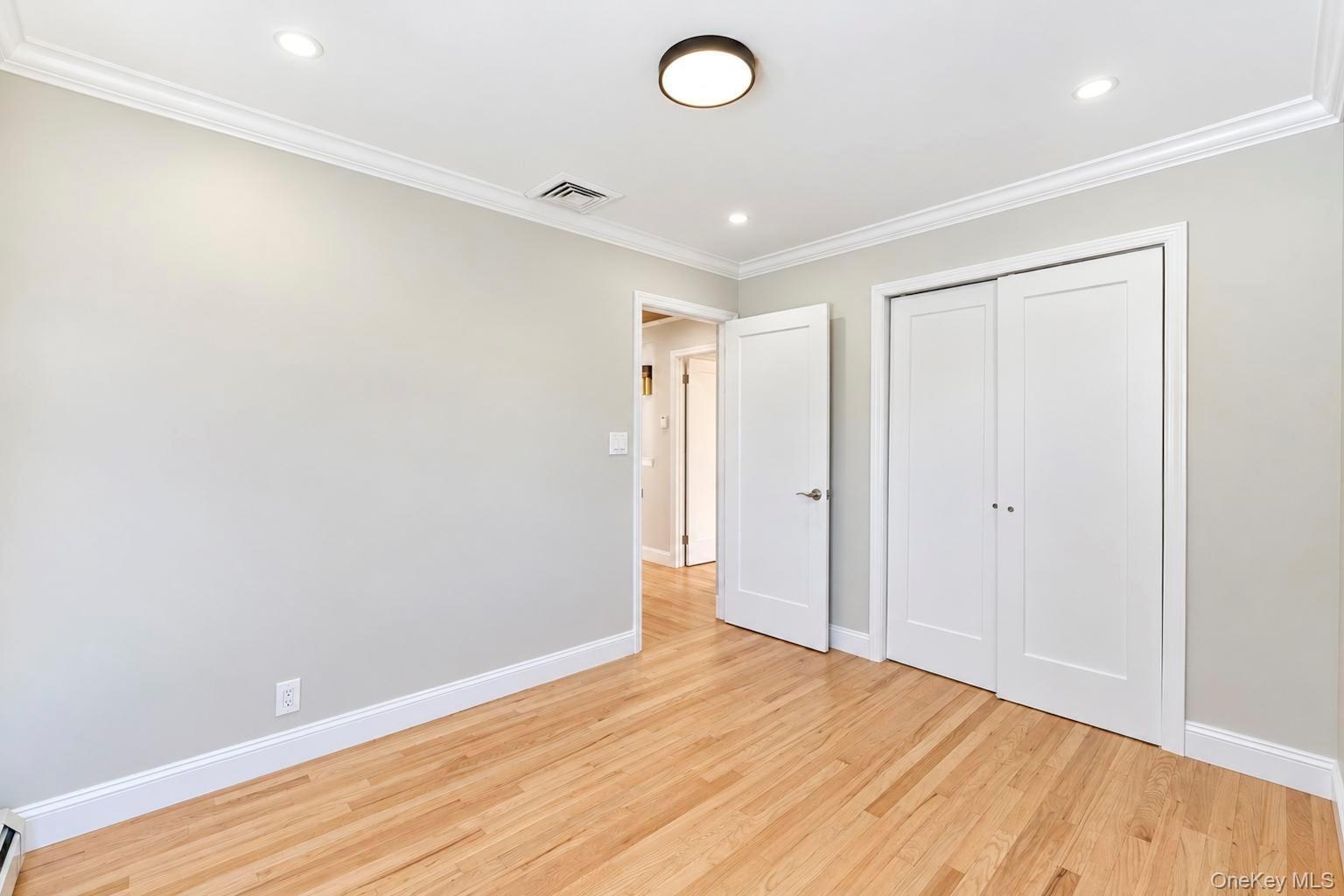 Neutral-toned interior featuring wood-finish flooring, crown molding, recessed lighting, and a double-door reach-in closet