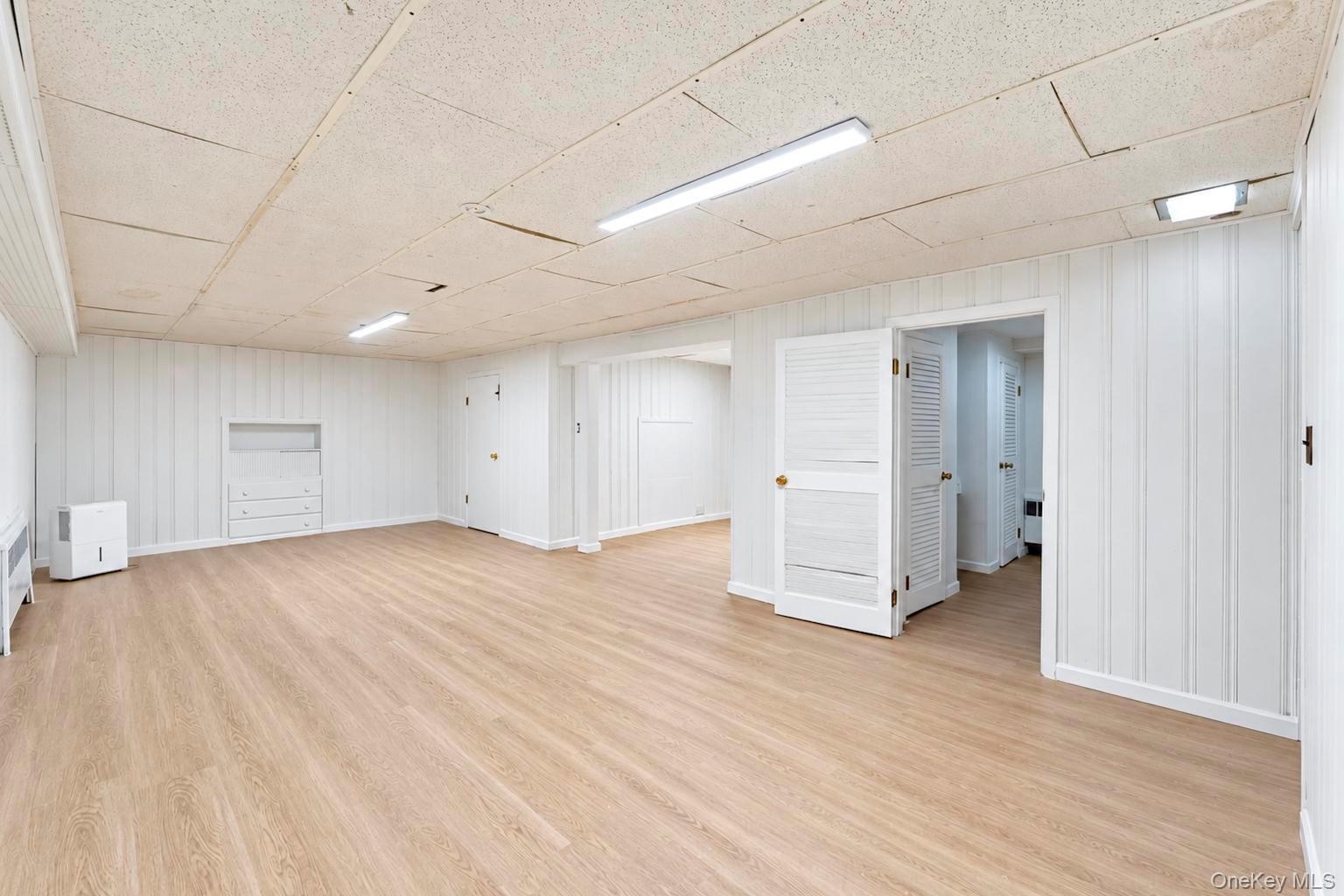 Interior space featuring vertical wood-paneled walls, wood-finish flooring, recessed built-in shelving, and louvered double doors
