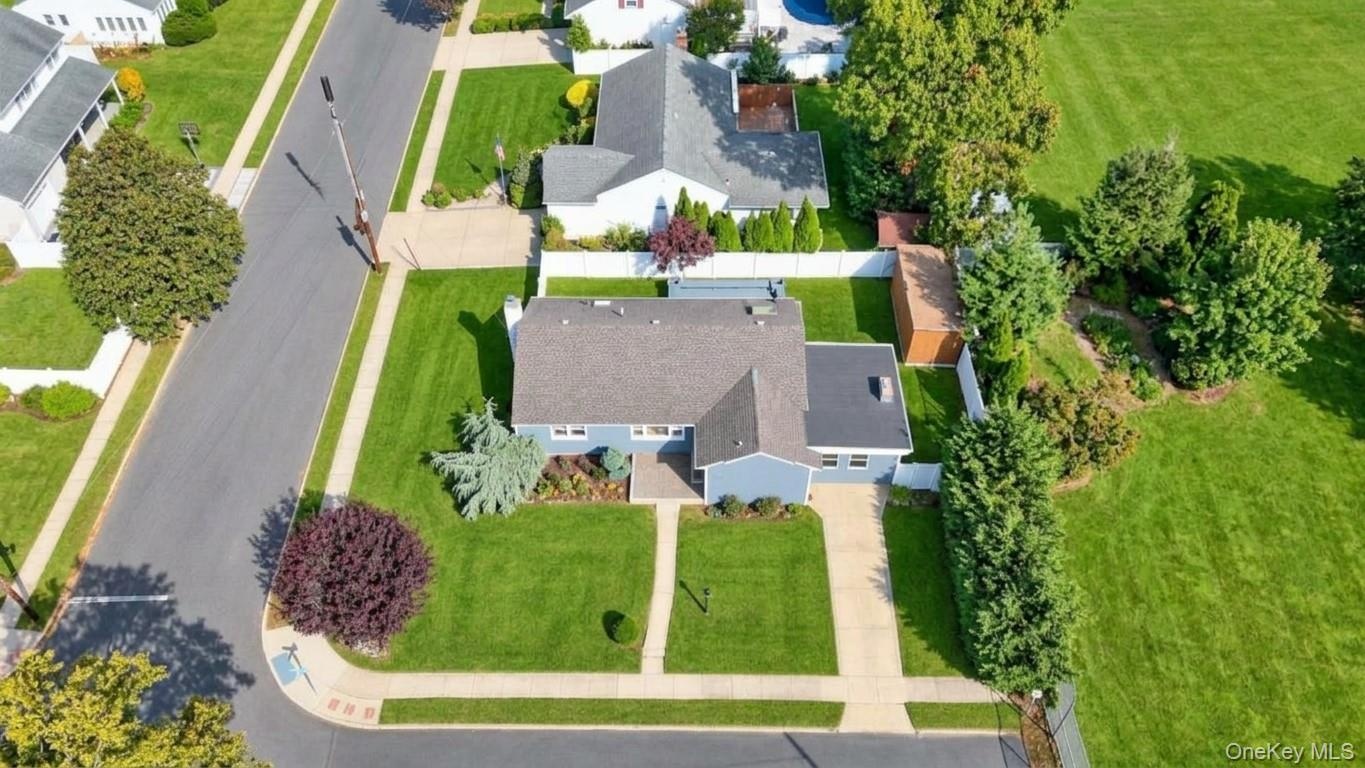 Aerial perspective featuring a corner lot, concrete driveway, stone walkway, exterior storage shed, and white privacy fencing