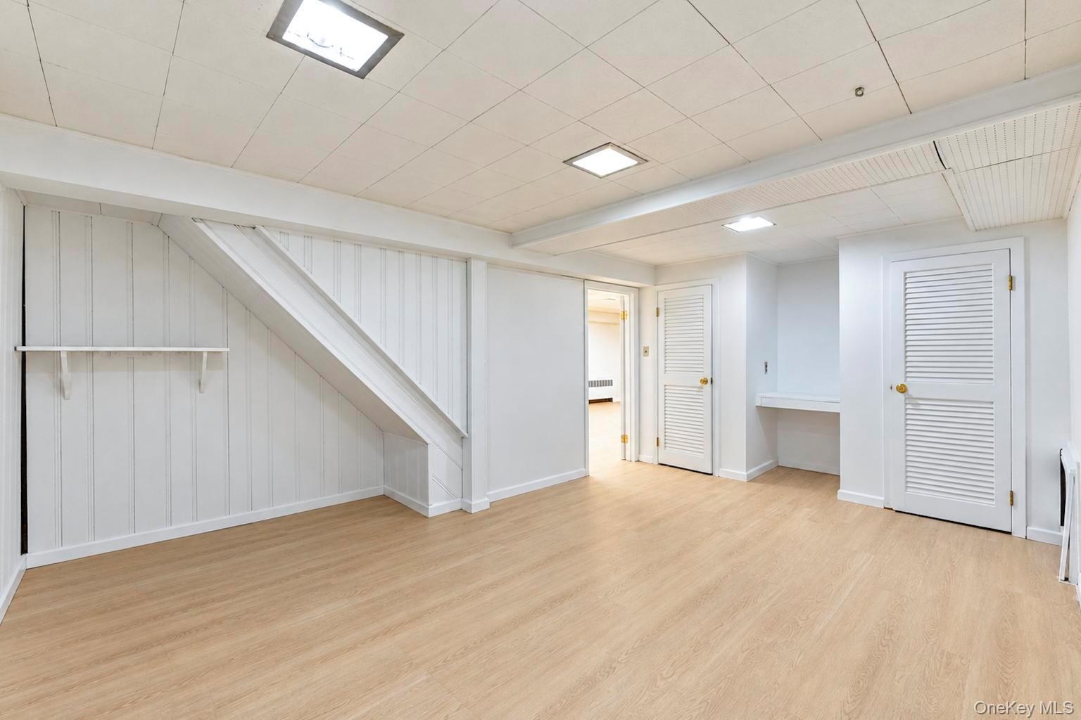 Interior space featuring wood-finish flooring, vertical panel wall detailing, recessed ceiling lighting, louvered closet doors, and built-in shelving