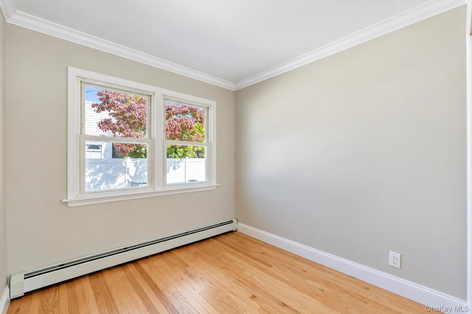Neutral-toned interior space featuring wood-finish flooring, double-pane windows, and crown molding