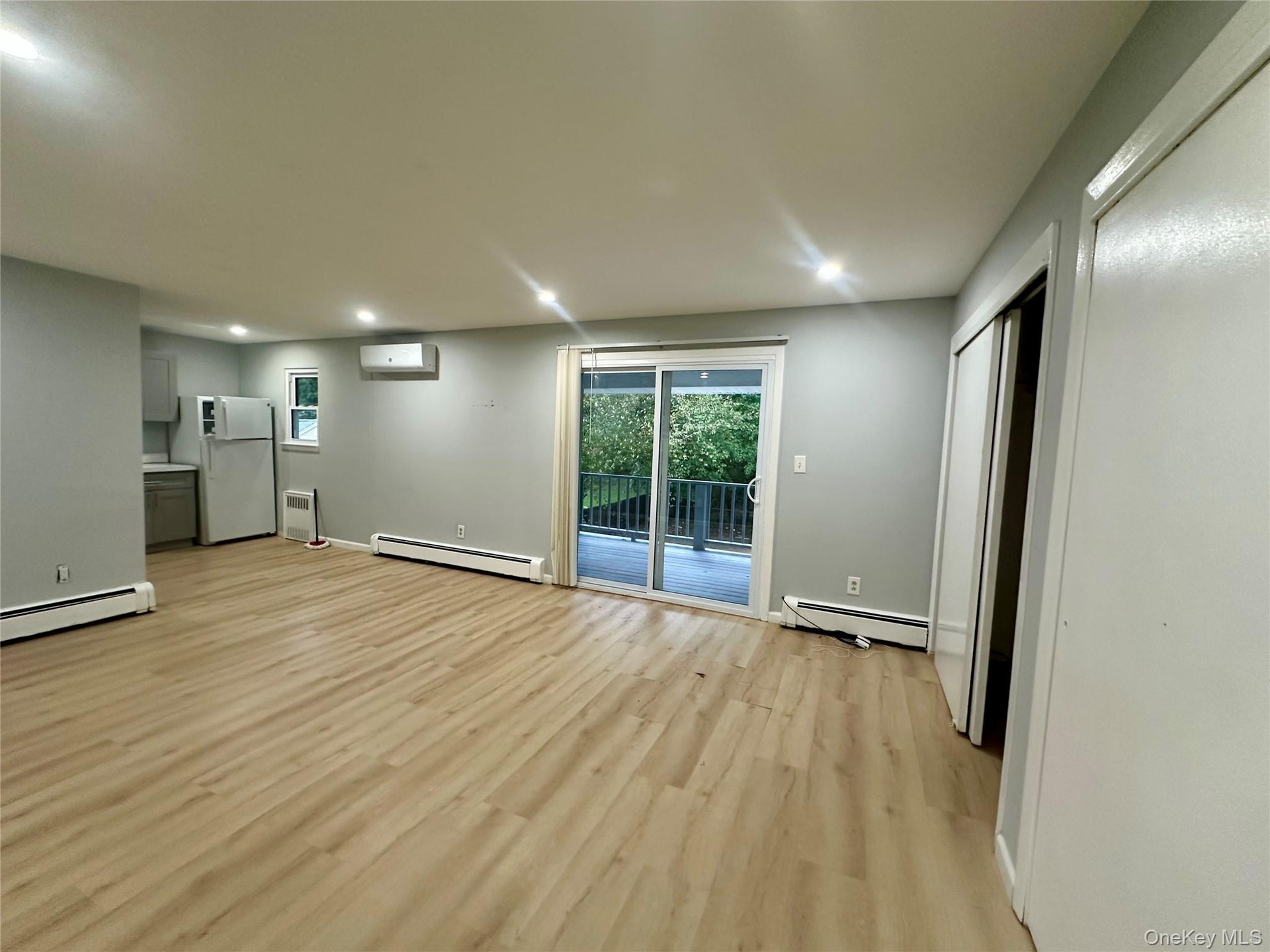 Open-concept interior featuring light wood-finish flooring, recessed lighting, sliding glass door, wall-mounted climate control unit, and closet with 