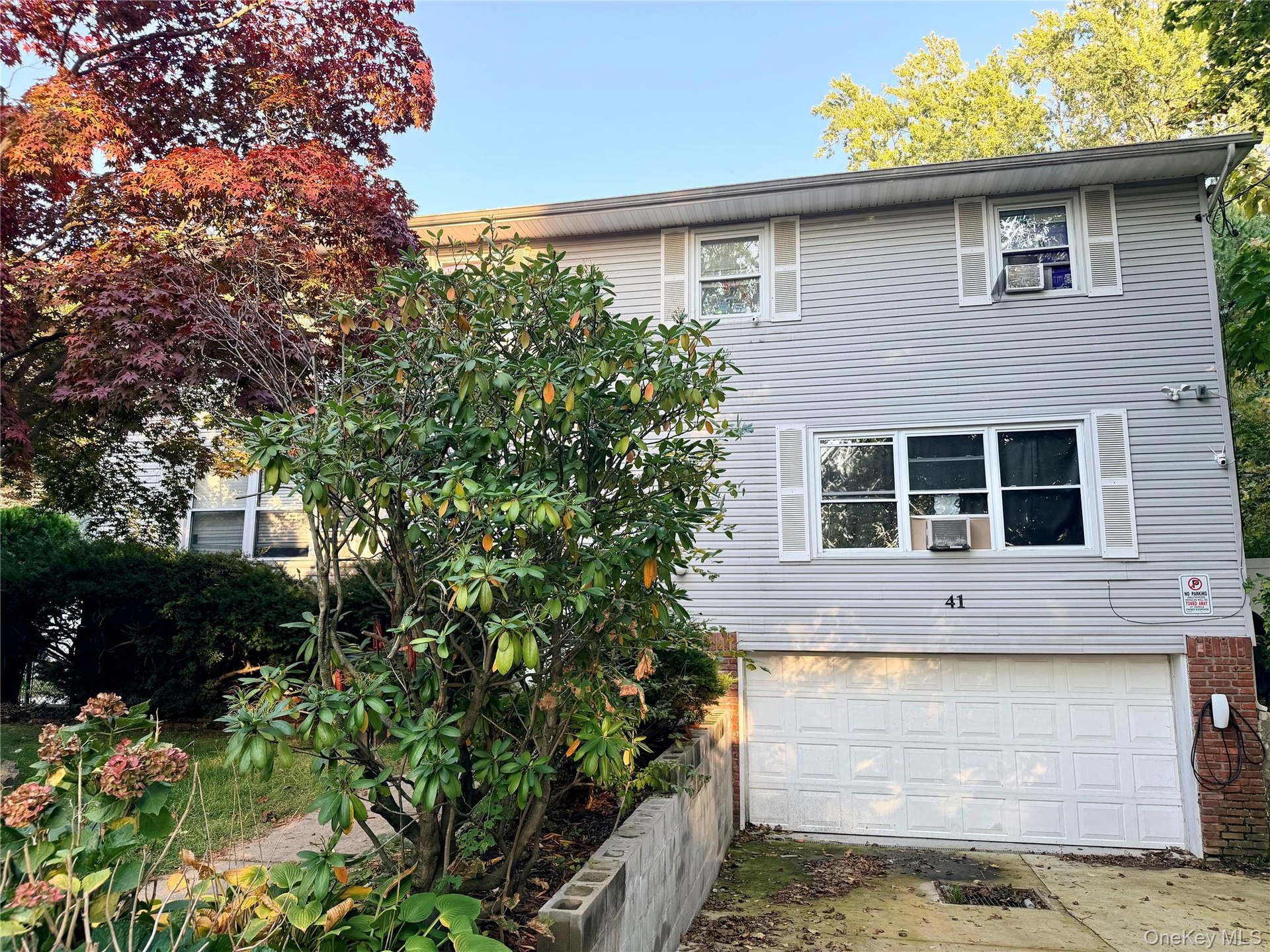 Two-story exterior featuring light-toned horizontal siding, decorative window shutters, a paved driveway, and an attached two-car garage
