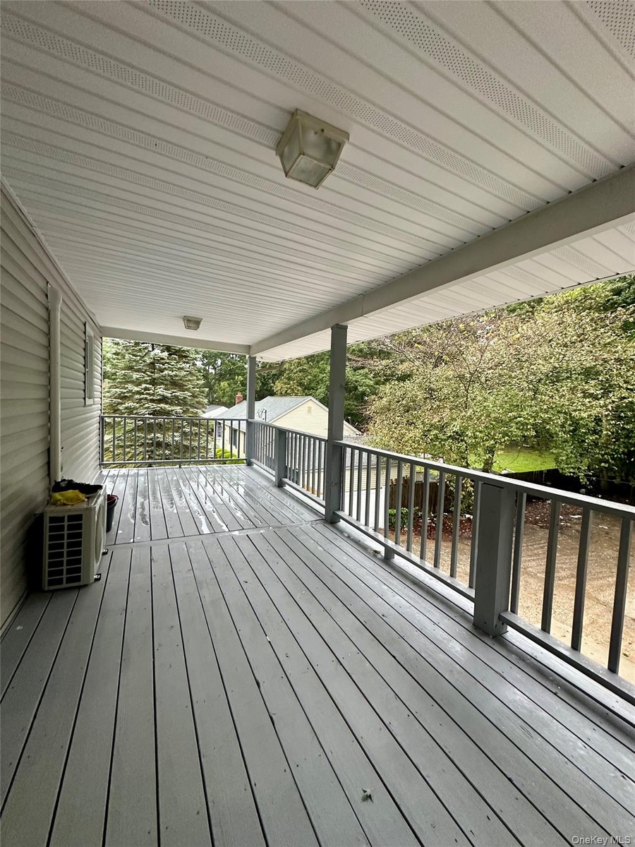 Covered balcony featuring painted wood-finish decking, structural support posts, and a full-length railing