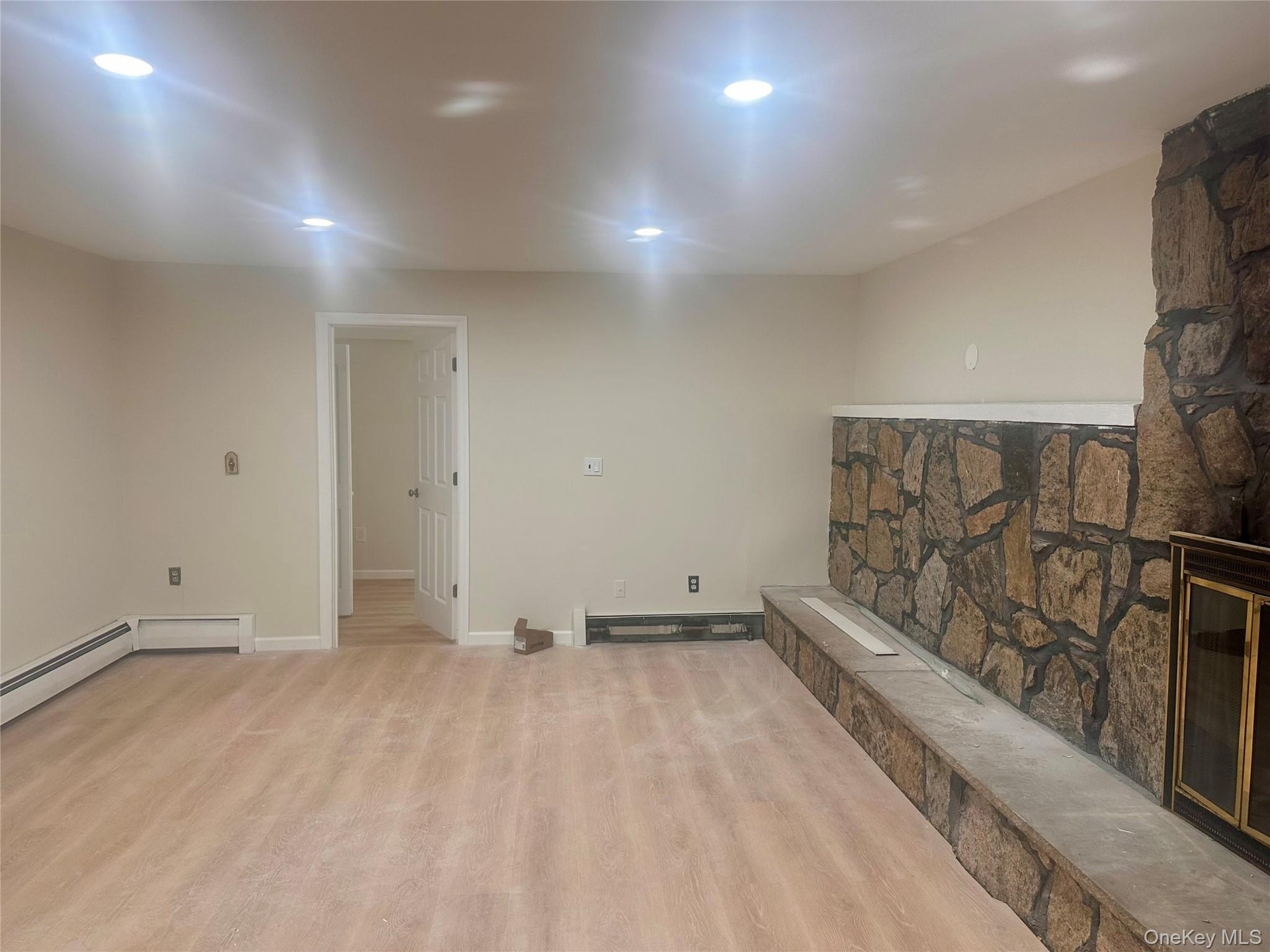 Stone fireplace with a raised hearth, wood-finish flooring, and recessed ceiling lighting