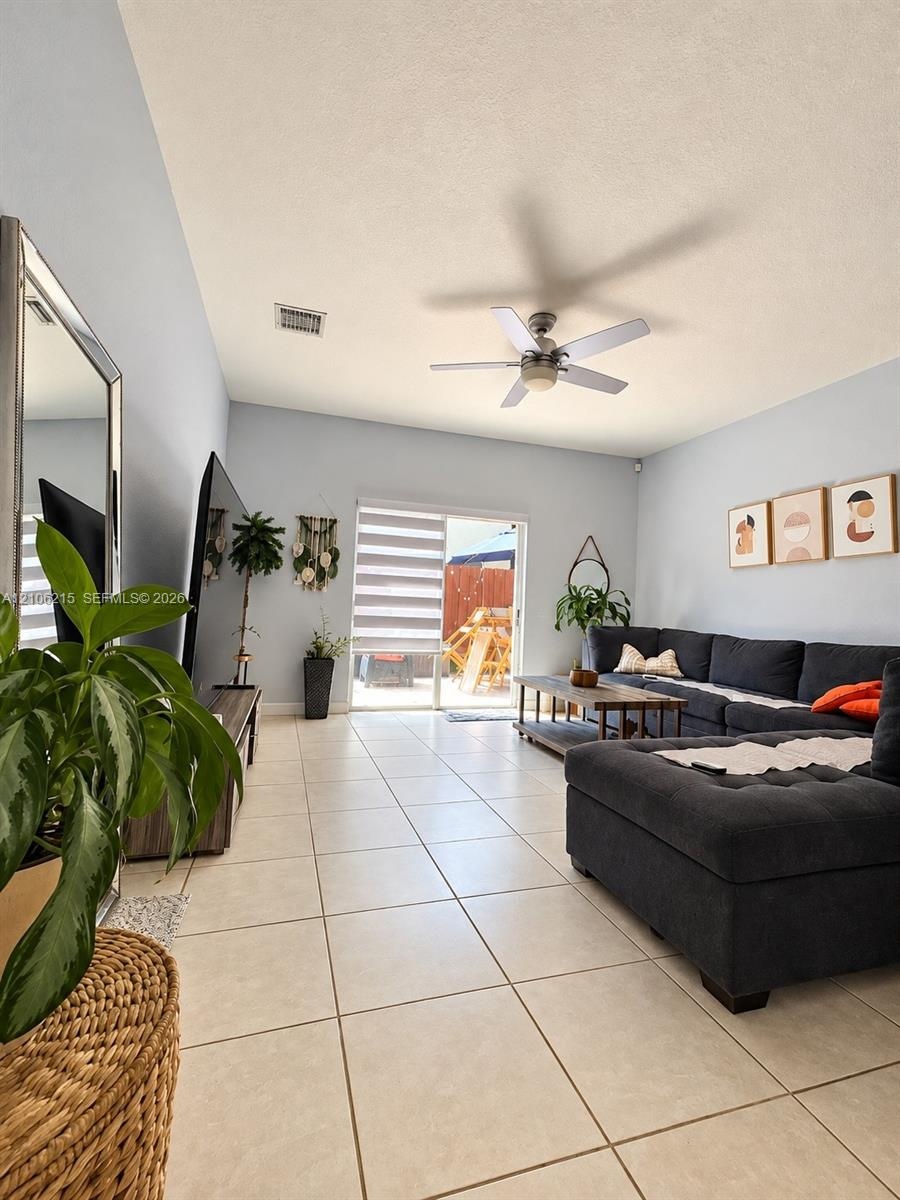 Living area featuring vaulted ceilings, light-tone tile flooring, a mounted ceiling fan, and sliding glass doors with roller shades