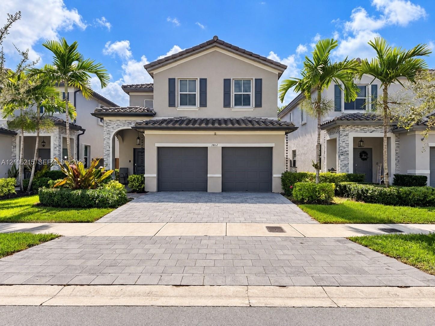 Two-story residence featuring a tile roof, neutral stucco exterior, stacked stone accents, and a paved two-car garage driveway