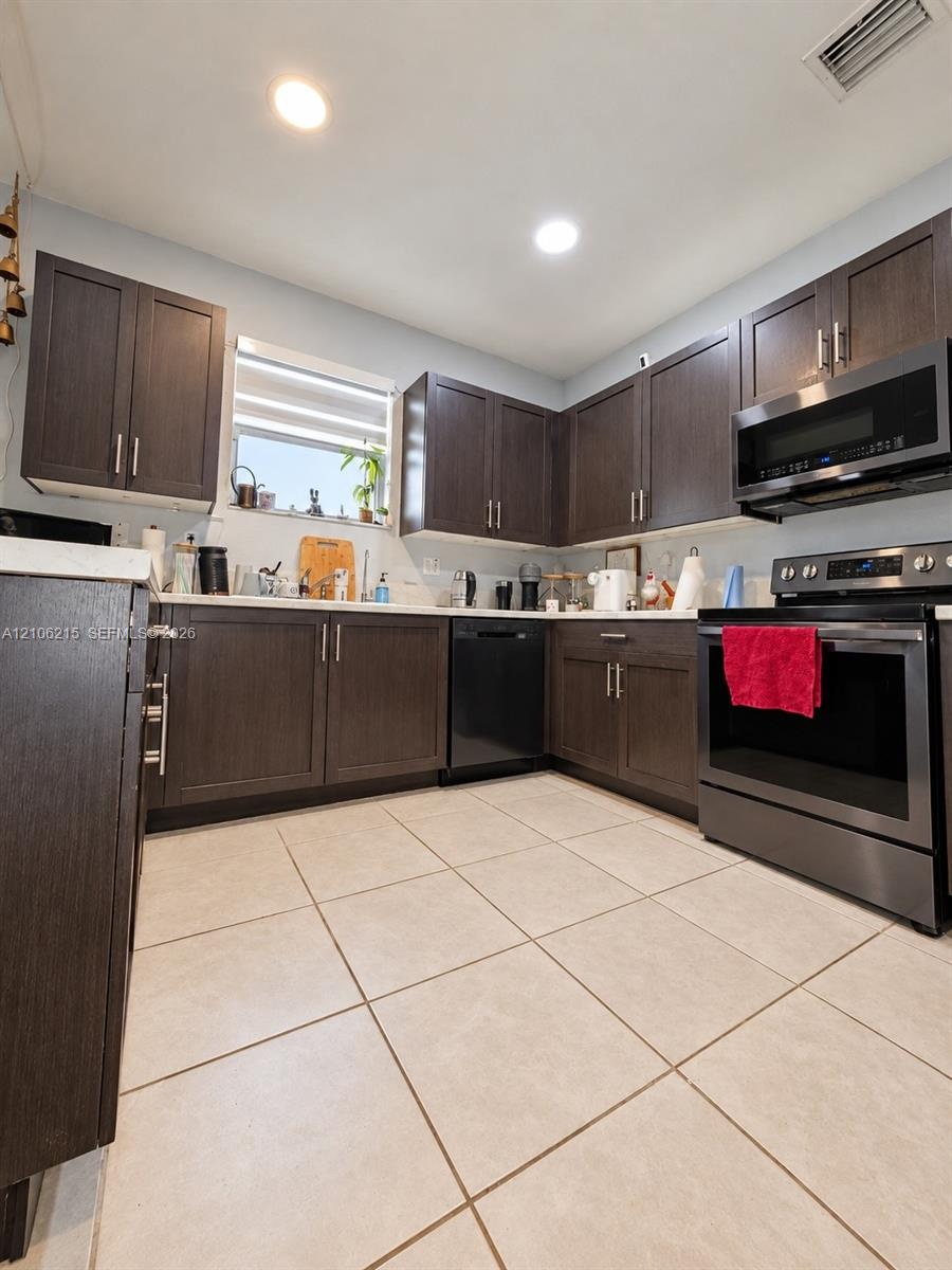 Kitchen featuring dark-finish cabinetry, solid-surface countertops, large-format tile flooring, and stainless steel appliances including a built-in mi